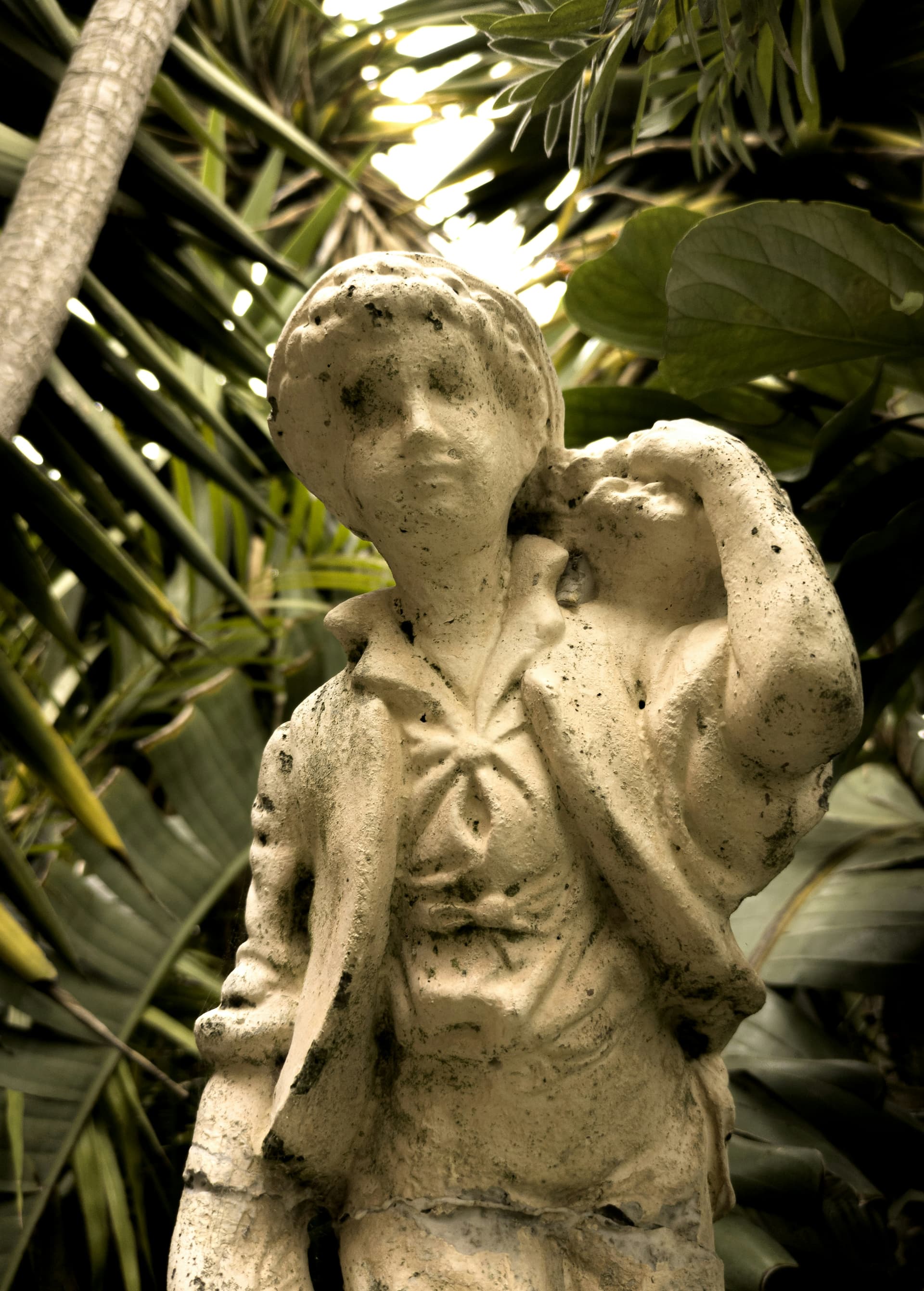 A weathered, pitted statue of a person carrying something - Image
