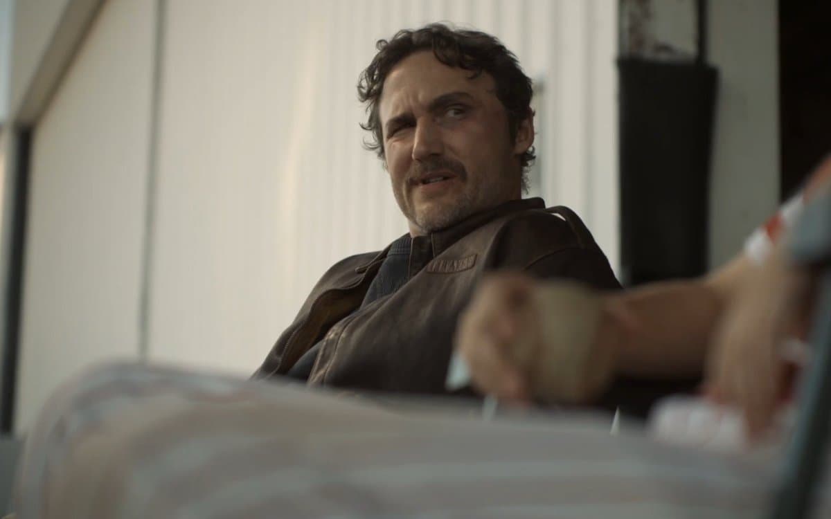 A mustachioed man in a brown leather jacket sits in a vehicle in a still from Lanterns.